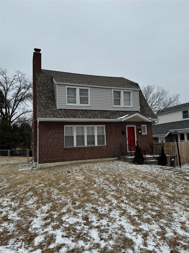 view of front facade featuring fence, a chimney, a shingled roof, and brick siding