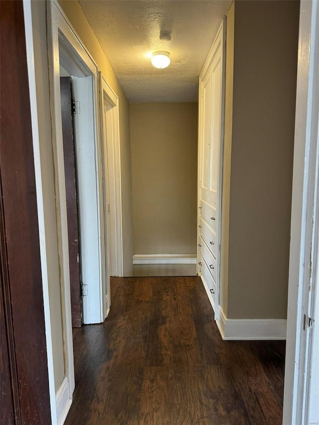 corridor featuring baseboards, a textured ceiling, and wood finished floors