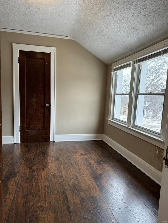 spare room with baseboards, vaulted ceiling, dark wood-style floors, and a textured ceiling