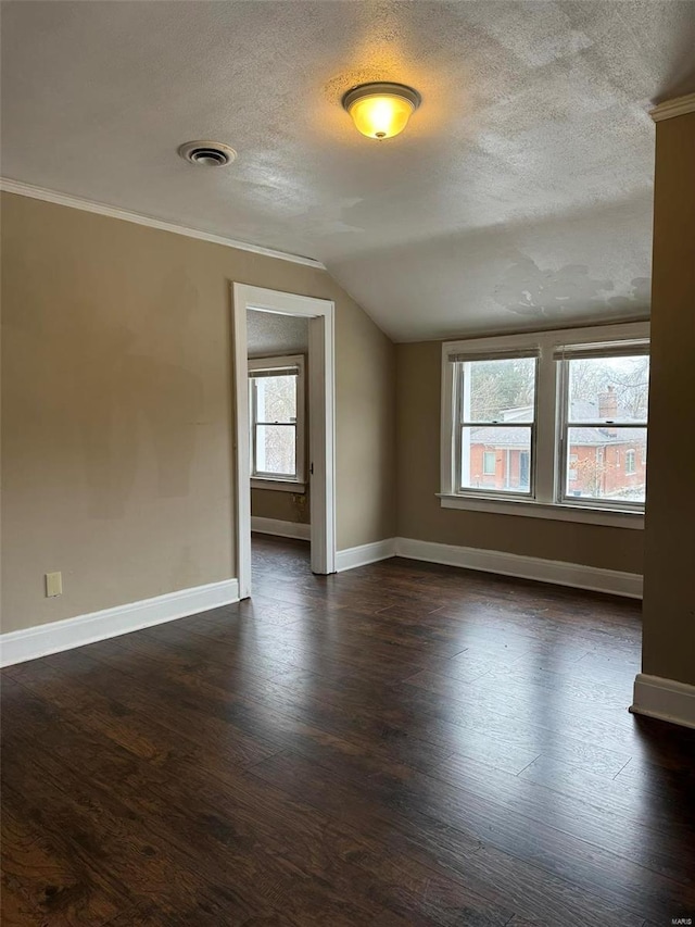 empty room with dark wood-style flooring, a textured ceiling, baseboards, vaulted ceiling, and visible vents