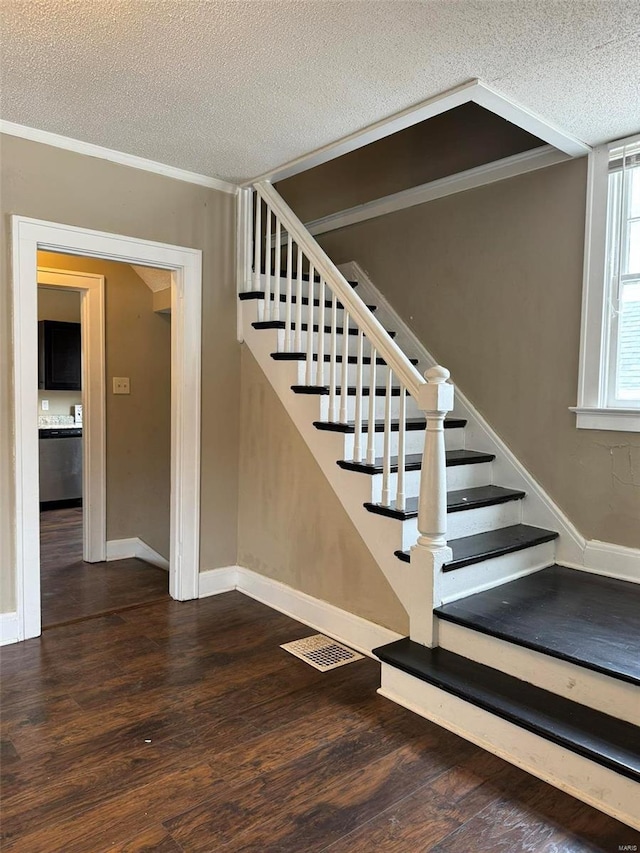 stairs featuring wood finished floors, baseboards, a textured ceiling, and visible vents
