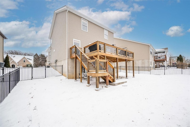 snow covered house with a fenced backyard, a deck, and stairs