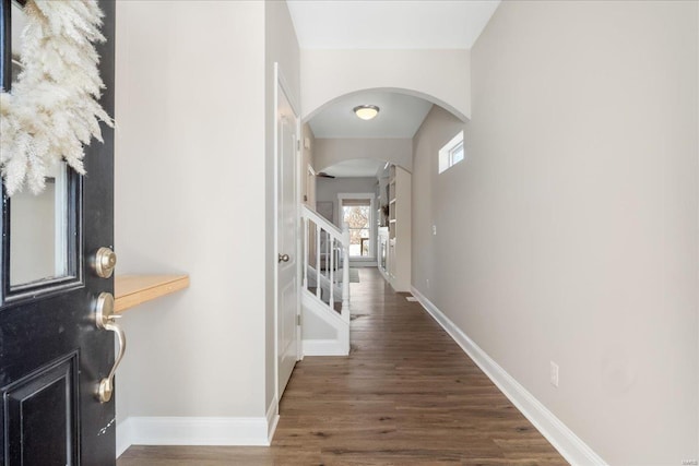 corridor with dark wood-type flooring, arched walkways, baseboards, and stairs