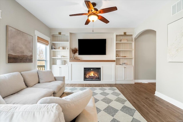 living area with baseboards, visible vents, arched walkways, a glass covered fireplace, and wood finished floors