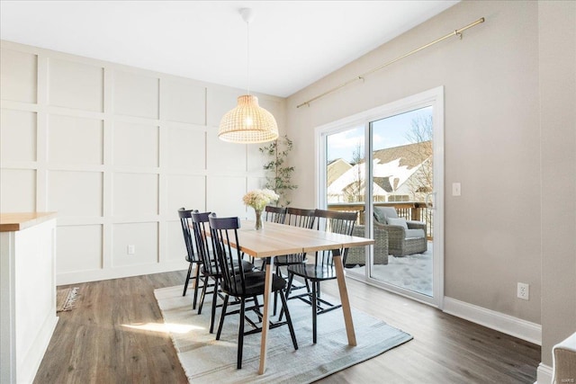 dining area featuring dark wood-style flooring, a decorative wall, and baseboards