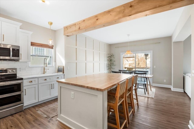 kitchen with decorative light fixtures, appliances with stainless steel finishes, white cabinets, a kitchen island, and a kitchen breakfast bar