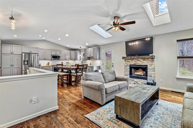 living area featuring lofted ceiling, a stone fireplace, recessed lighting, baseboards, and dark wood finished floors