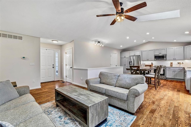 living room featuring visible vents, vaulted ceiling, ceiling fan, light wood-type flooring, and baseboards