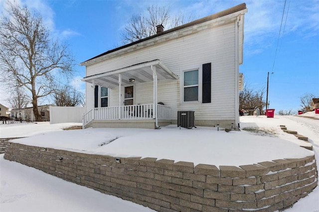 snow covered property with a chimney, central AC unit, and a porch