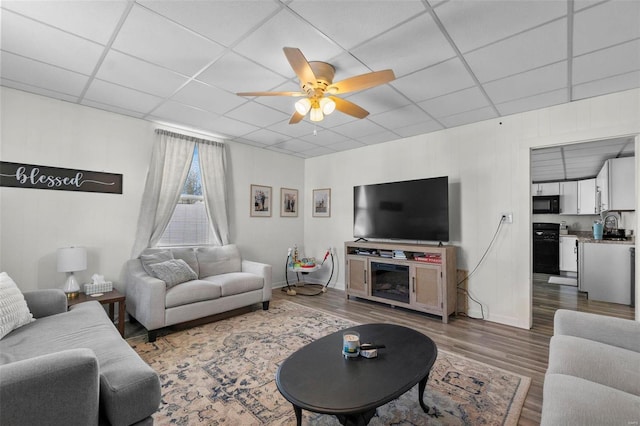 living area featuring a paneled ceiling, ceiling fan, baseboards, and wood finished floors