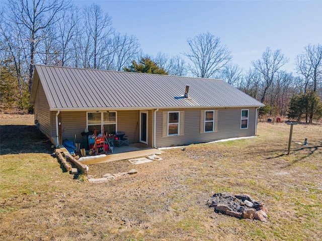 view of front facade with metal roof, an outdoor fire pit, a front lawn, and a patio area