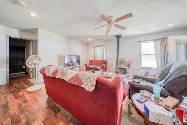 living area with a wood stove, a textured ceiling, a ceiling fan, and wood finished floors