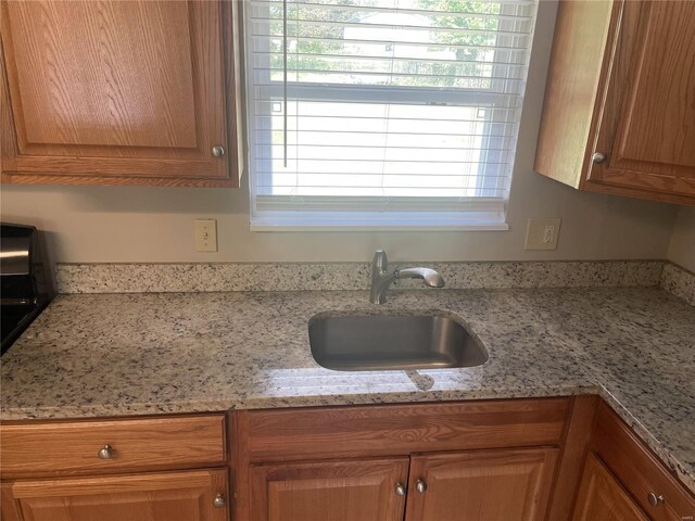 kitchen with light stone counters, brown cabinetry, and a sink