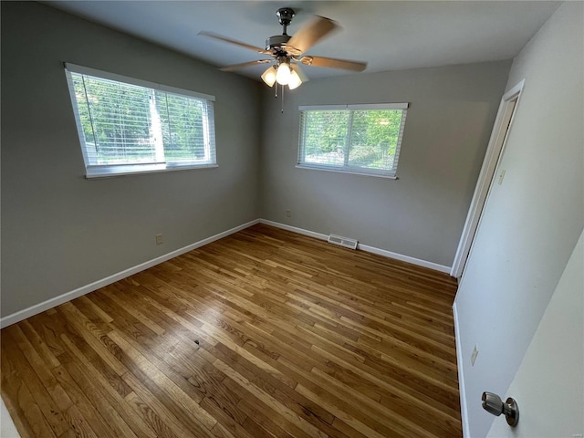 unfurnished bedroom featuring baseboards, multiple windows, visible vents, and wood finished floors
