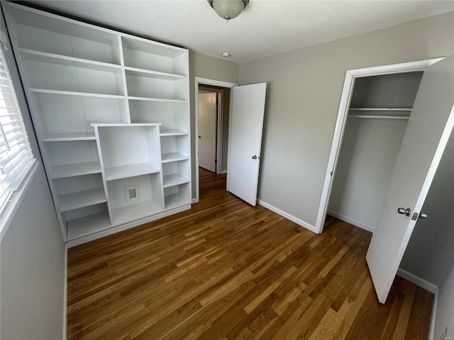 unfurnished bedroom featuring a closet, dark wood-style flooring, and baseboards