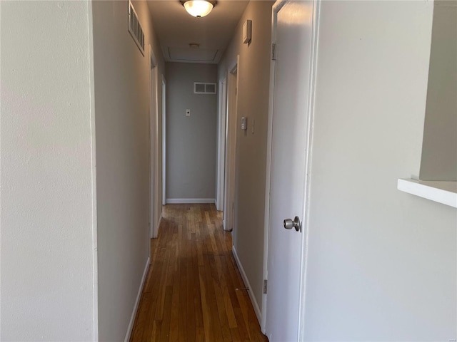 hallway featuring dark wood-type flooring, visible vents, and baseboards