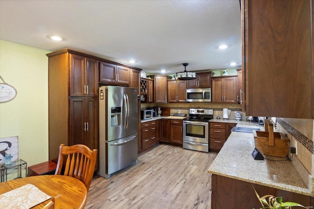 kitchen with light hardwood / wood-style floors, sink, tasteful backsplash, light stone counters, and appliances with stainless steel finishes