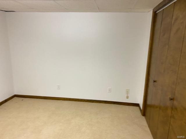 unfurnished bedroom with a paneled ceiling, a closet, and light colored carpet