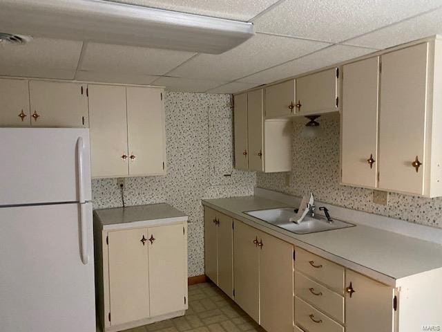 kitchen with white refrigerator, sink, a paneled ceiling, and cream cabinetry