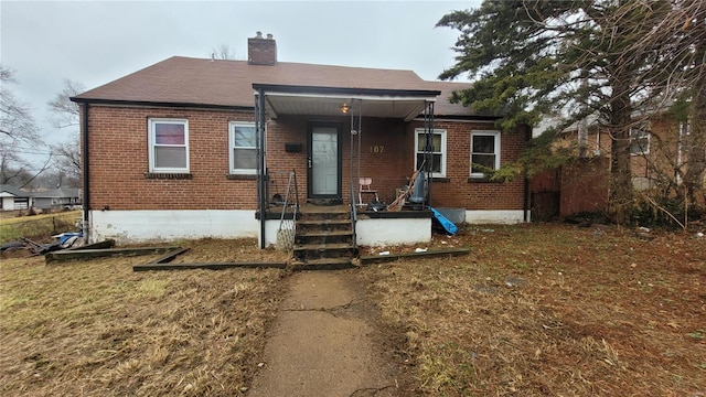 bungalow-style home with brick siding, a front yard, and a chimney