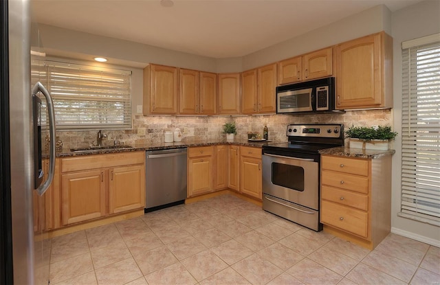 kitchen with a sink, stainless steel appliances, backsplash, and light brown cabinetry