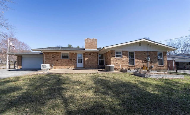 rear view of house featuring fence, a chimney, concrete driveway, a lawn, and brick siding