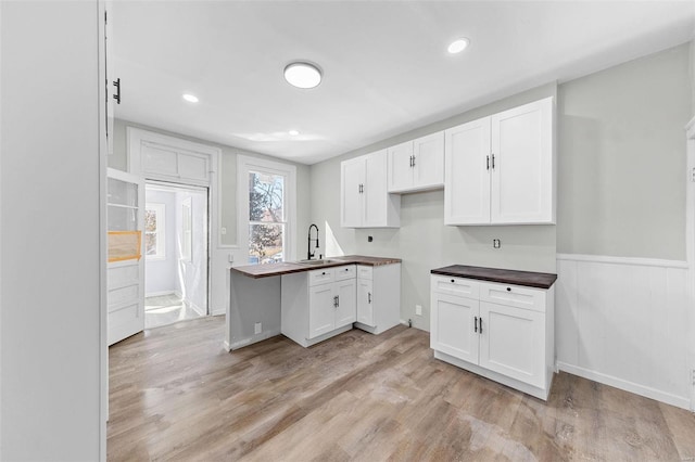 kitchen with wainscoting, white cabinets, a sink, and light wood-style flooring