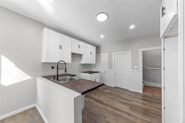 kitchen featuring dark wood finished floors, dark countertops, a peninsula, white cabinetry, and a sink