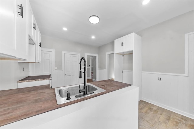 kitchen featuring recessed lighting, a wainscoted wall, a sink, white cabinetry, and light wood-style floors
