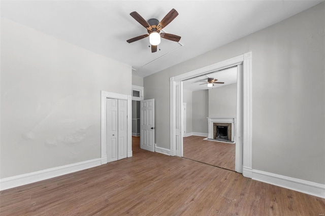 unfurnished bedroom with ceiling fan, a fireplace, wood finished floors, and baseboards