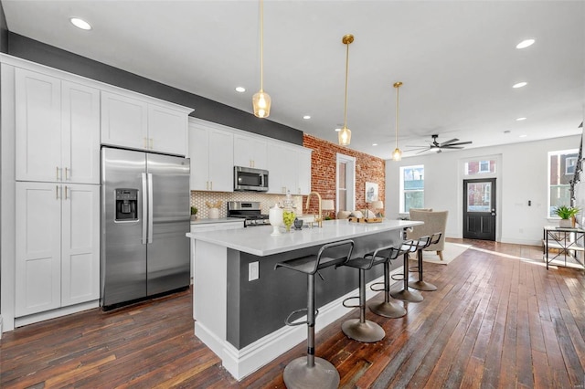 kitchen with appliances with stainless steel finishes, pendant lighting, dark hardwood / wood-style flooring, a kitchen island, and white cabinetry