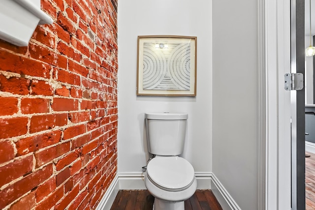 bathroom featuring wood-type flooring, brick wall, and toilet