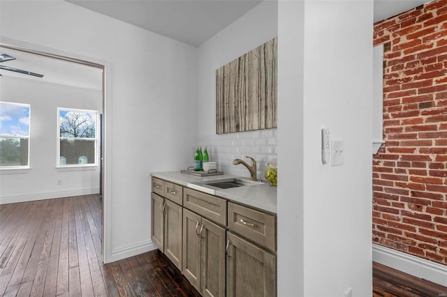 bar featuring brick wall, sink, dark wood-type flooring, and backsplash