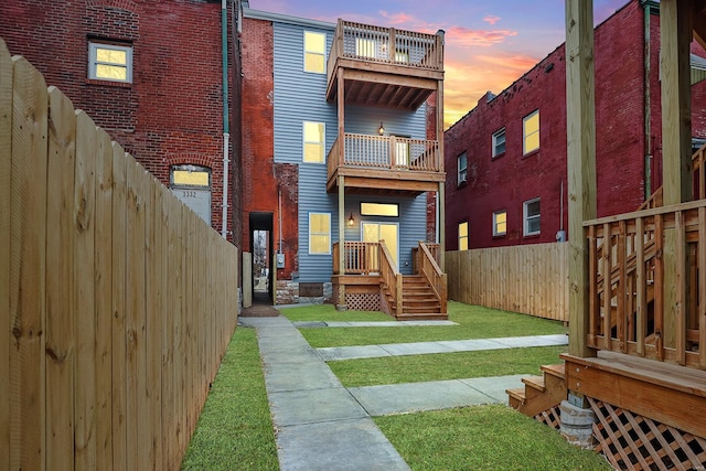 back house at dusk featuring a balcony and a lawn