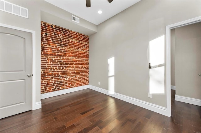 unfurnished room featuring ceiling fan, dark hardwood / wood-style flooring, and brick wall