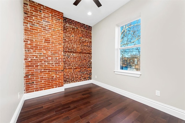 empty room with hardwood / wood-style floors, ceiling fan, and brick wall