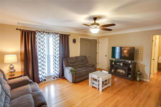 living area featuring light wood-style floors, a glass covered fireplace, baseboards, and a ceiling fan