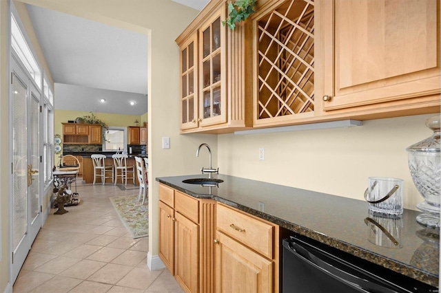 kitchen with light tile patterned floors, black dishwasher, dark stone counters, glass insert cabinets, and a sink