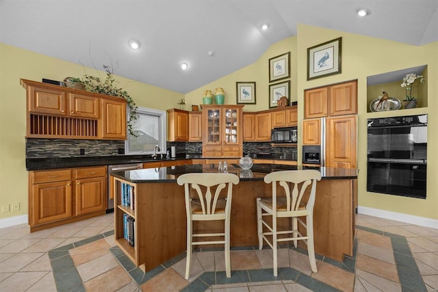 kitchen with brown cabinets, open shelves, a sink, an island with sink, and black appliances