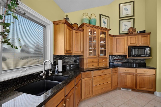 kitchen featuring glass insert cabinets, black microwave, brown cabinetry, and dark stone countertops