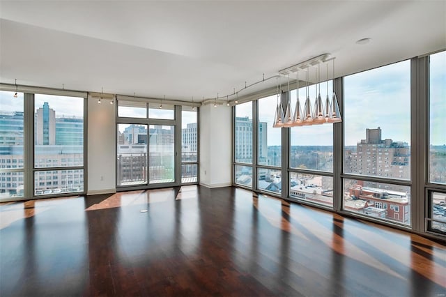 spare room featuring baseboards, a wall of windows, wood finished floors, and a city view