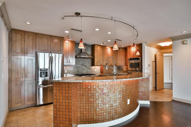 kitchen with stone counters, decorative backsplash, appliances with stainless steel finishes, brown cabinetry, and wall chimney range hood