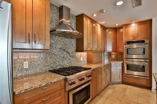 kitchen featuring stainless steel appliances, visible vents, wall chimney range hood, and light stone countertops