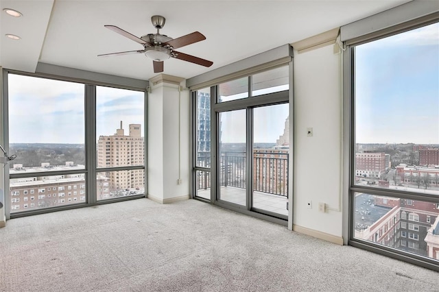 carpeted empty room featuring a ceiling fan, a view of city, baseboards, and expansive windows