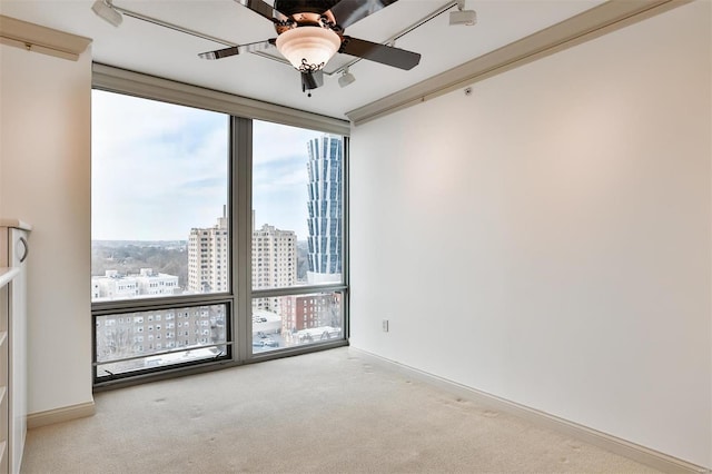 unfurnished room featuring a view of city, carpet, a ceiling fan, a wall of windows, and baseboards