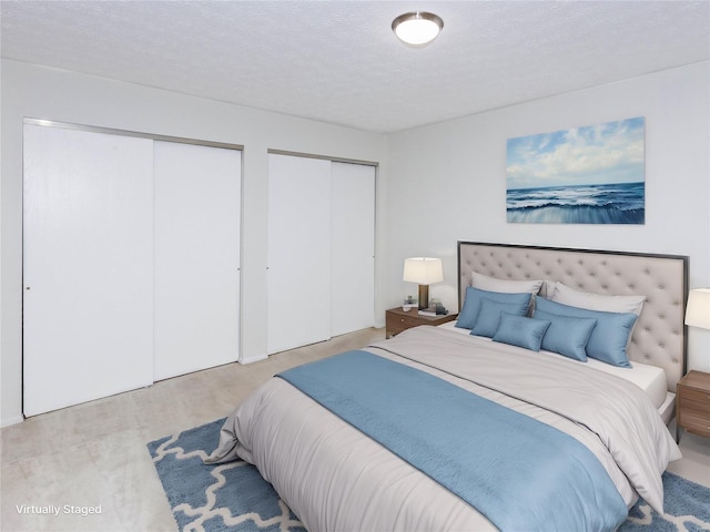 bedroom featuring light wood-type flooring, multiple closets, and a textured ceiling