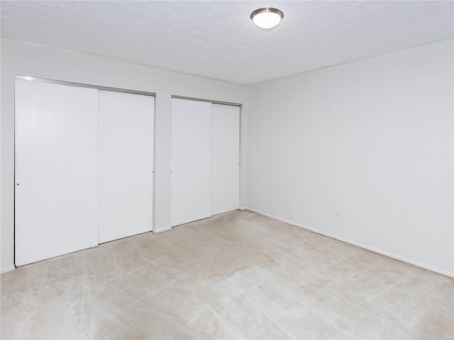 unfurnished bedroom featuring a textured ceiling and two closets