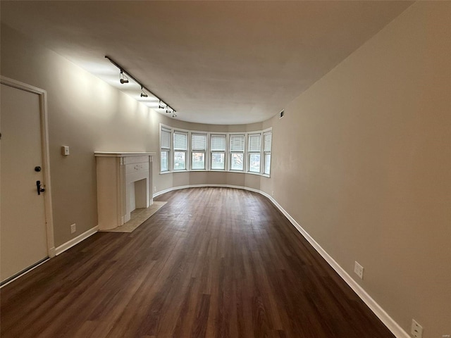 unfurnished living room with dark wood-type flooring, baseboards, a high end fireplace, and track lighting