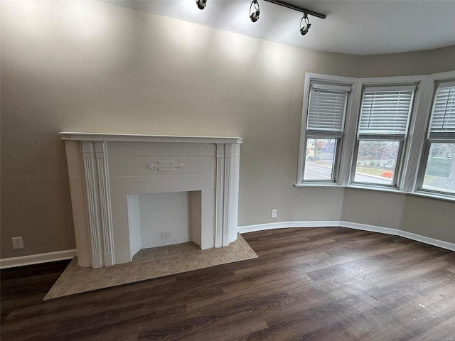 unfurnished living room featuring baseboards, track lighting, and dark wood-style flooring