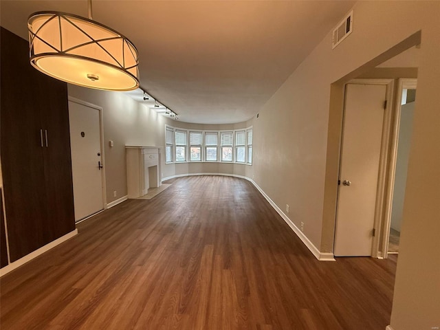 unfurnished living room featuring track lighting, wood finished floors, visible vents, and baseboards